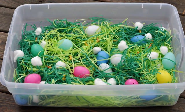 Easter-themed sensory bin with plastic eggs and Easter grass